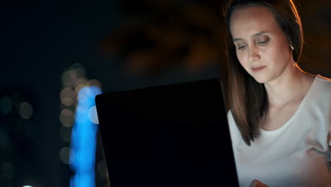 Young-beautiful-girl-designer-working-remotely-on-a-laptop-on-the-street-in-the-summer-under-palm-trees-at-night-in-the-city-Park.-United-Arab-Emirates-European-woman-at-night-in-Dubai
